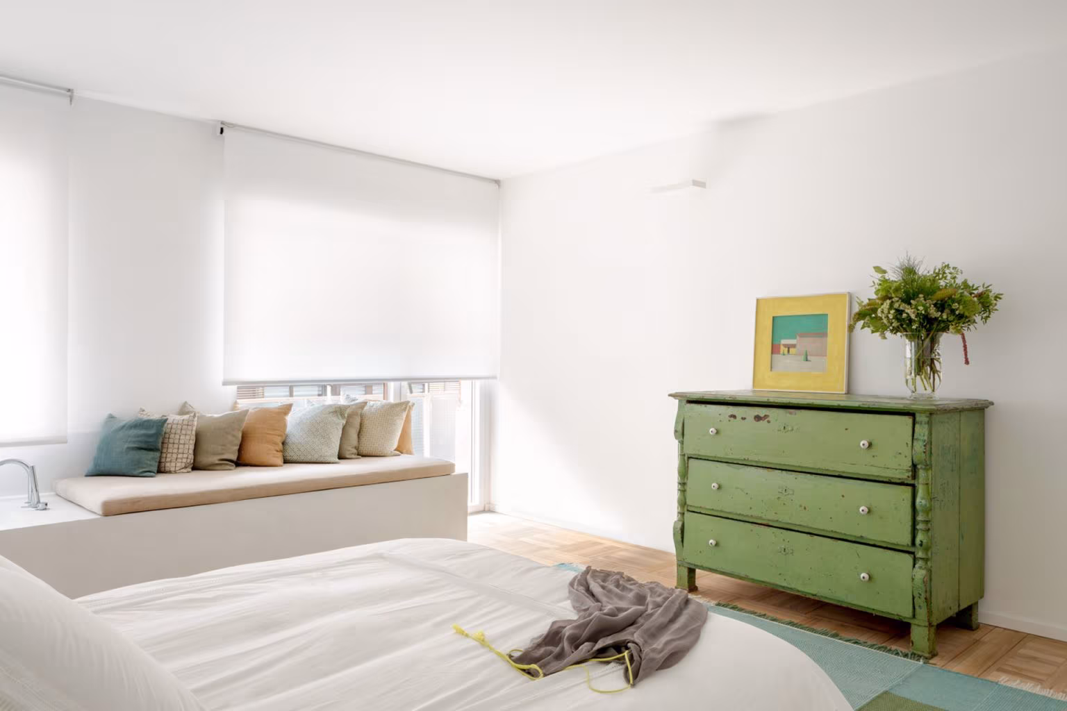 Dormitorio con cómoda verde, banco con cojines y estores de lino, en la reforma integral del Barrio de Salamanca
