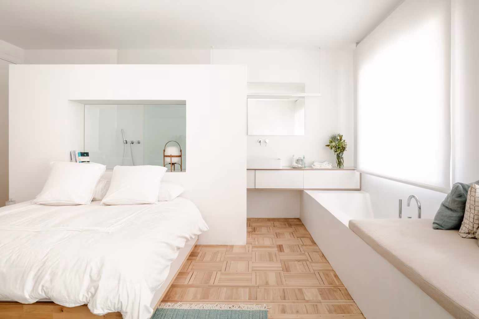 Dormitorio abierto a un baño tras un tabique blanco, con bañera sobre tarima y suelo de parqué, en Salamanca