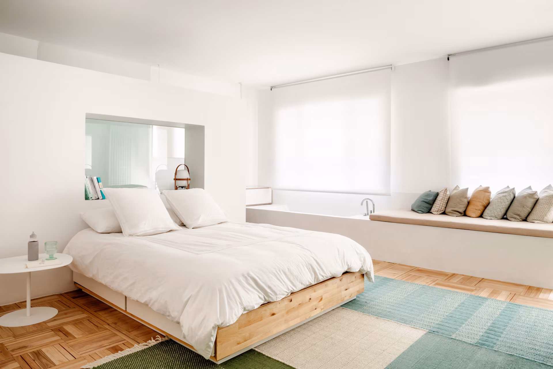 Dormitorio con cama de madera, banco corrido bajo la ventana y alfombra verde sobre parqué, en el Barrio de Salamanca
