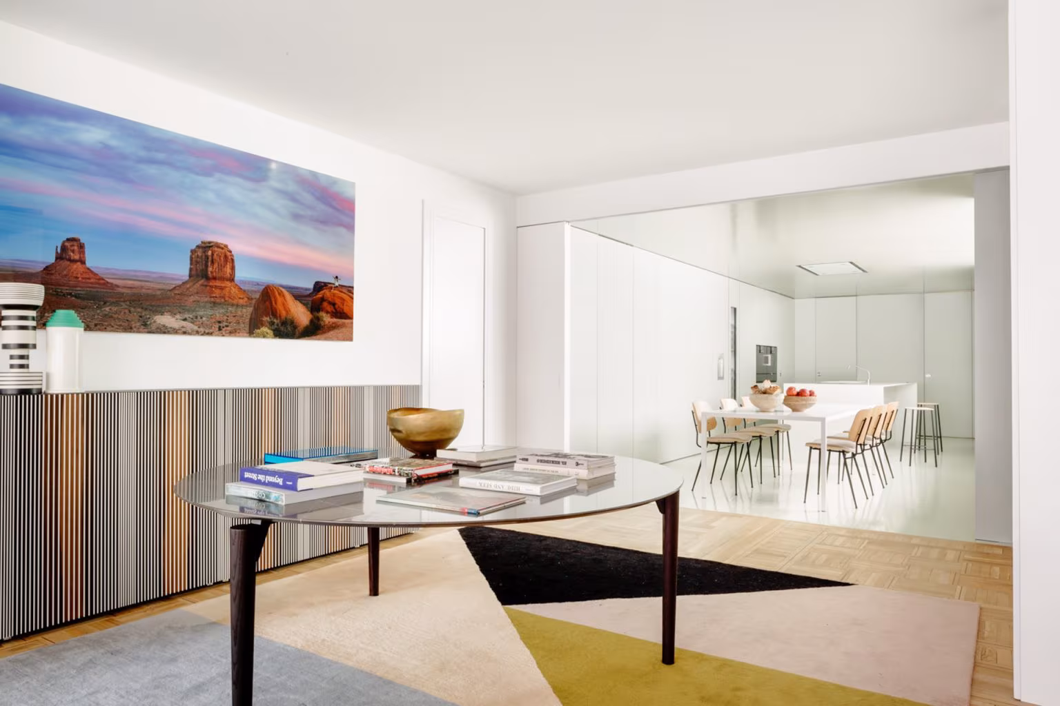 Mueble de lamas de colores bajo un paisaje fotográfico, mesa ovalada y alfombra geométrica, en el Barrio de Salamanca