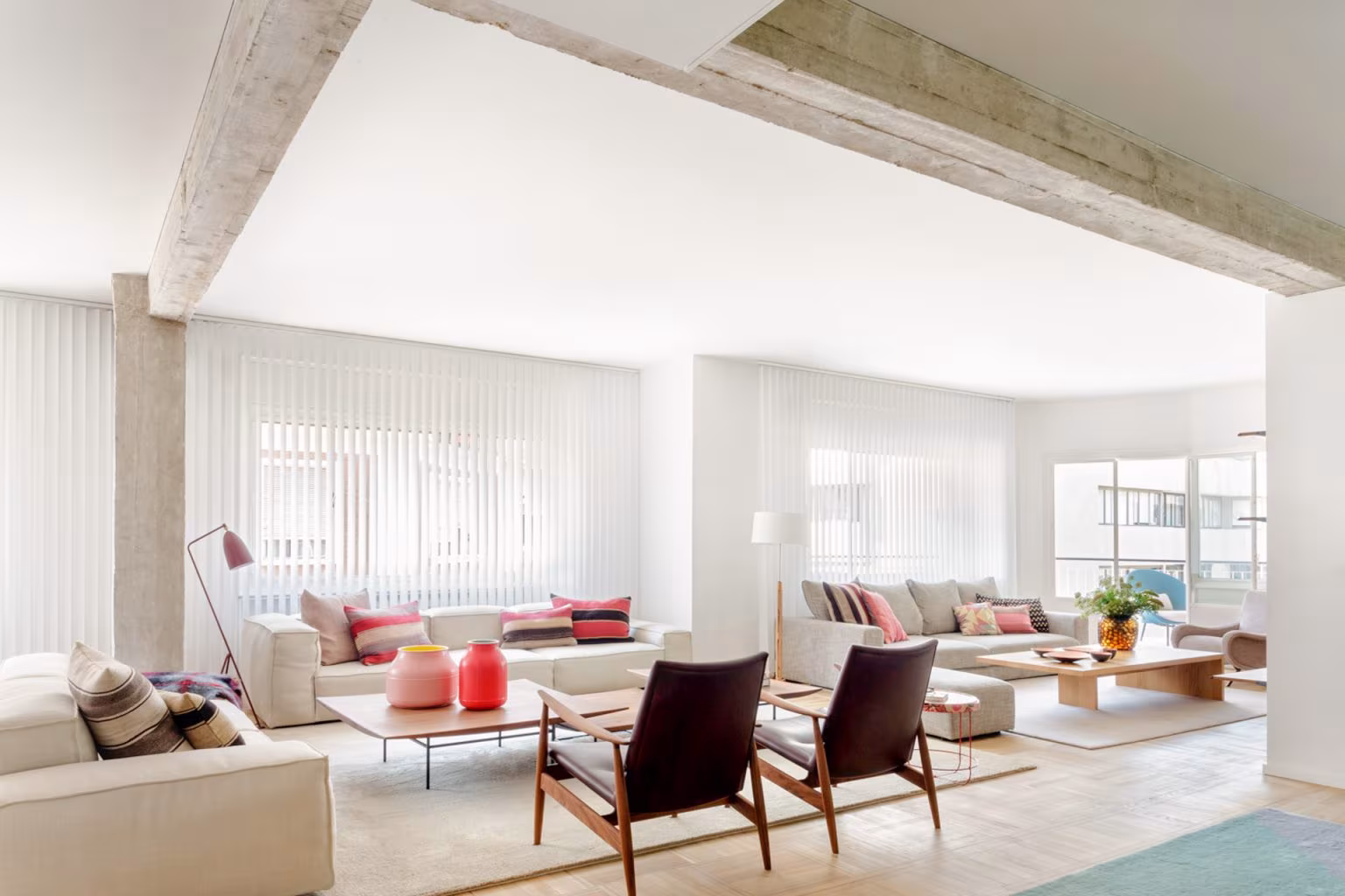 Salón amplio con vigas de hormigón vistas, sofás claros y butacas de madera en el Barrio de Salamanca, obra de Ábaton