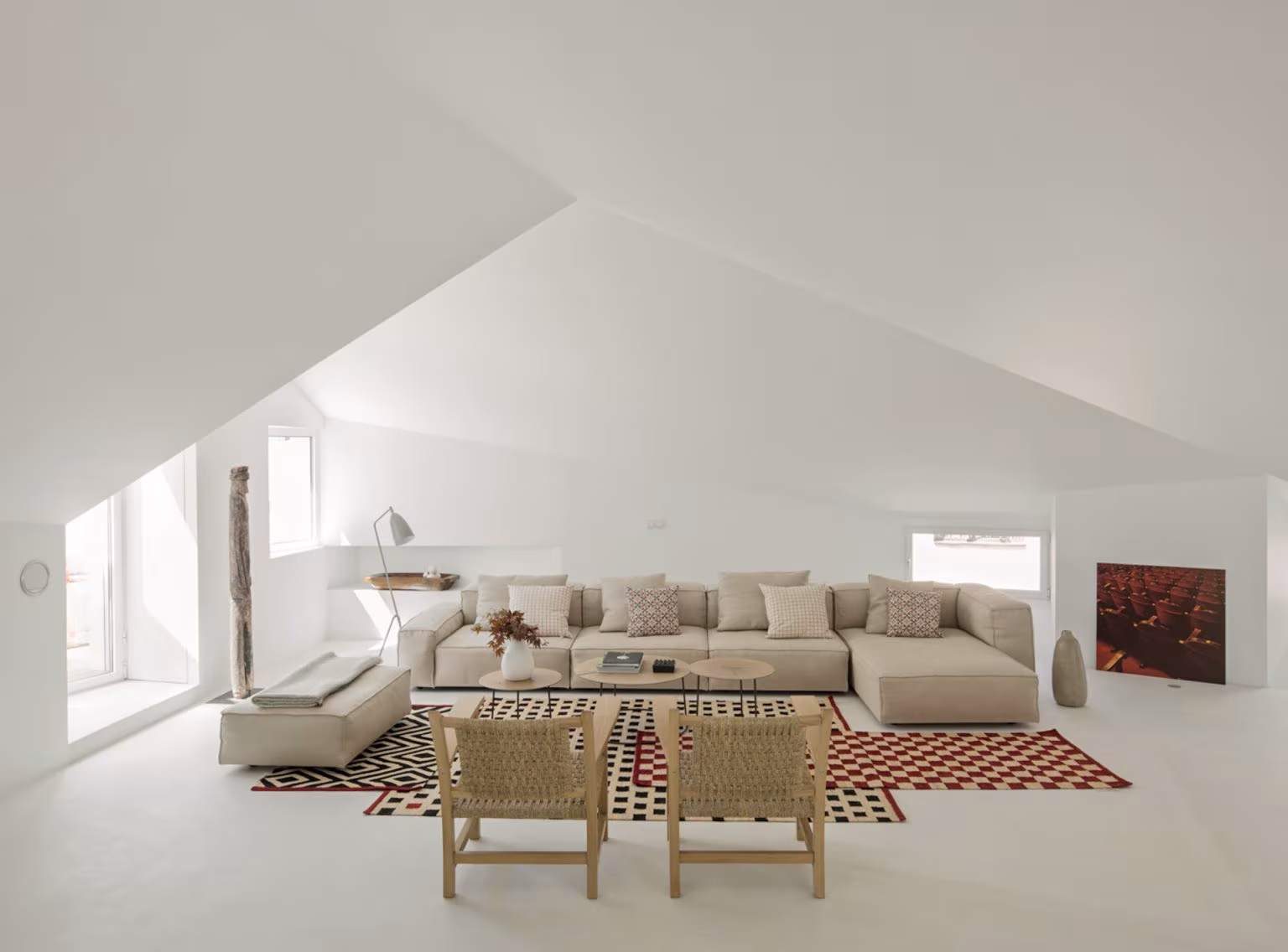 Sala diáfana bajo una cubierta de planos inclinados blancos con sofá modular y alfombra geométrica, en Alcalá