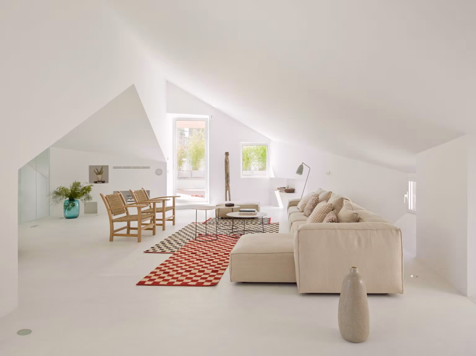 Living room under a white broken roof with sofa, rush armchairs and a red check rug in the Alcalá refurbishment