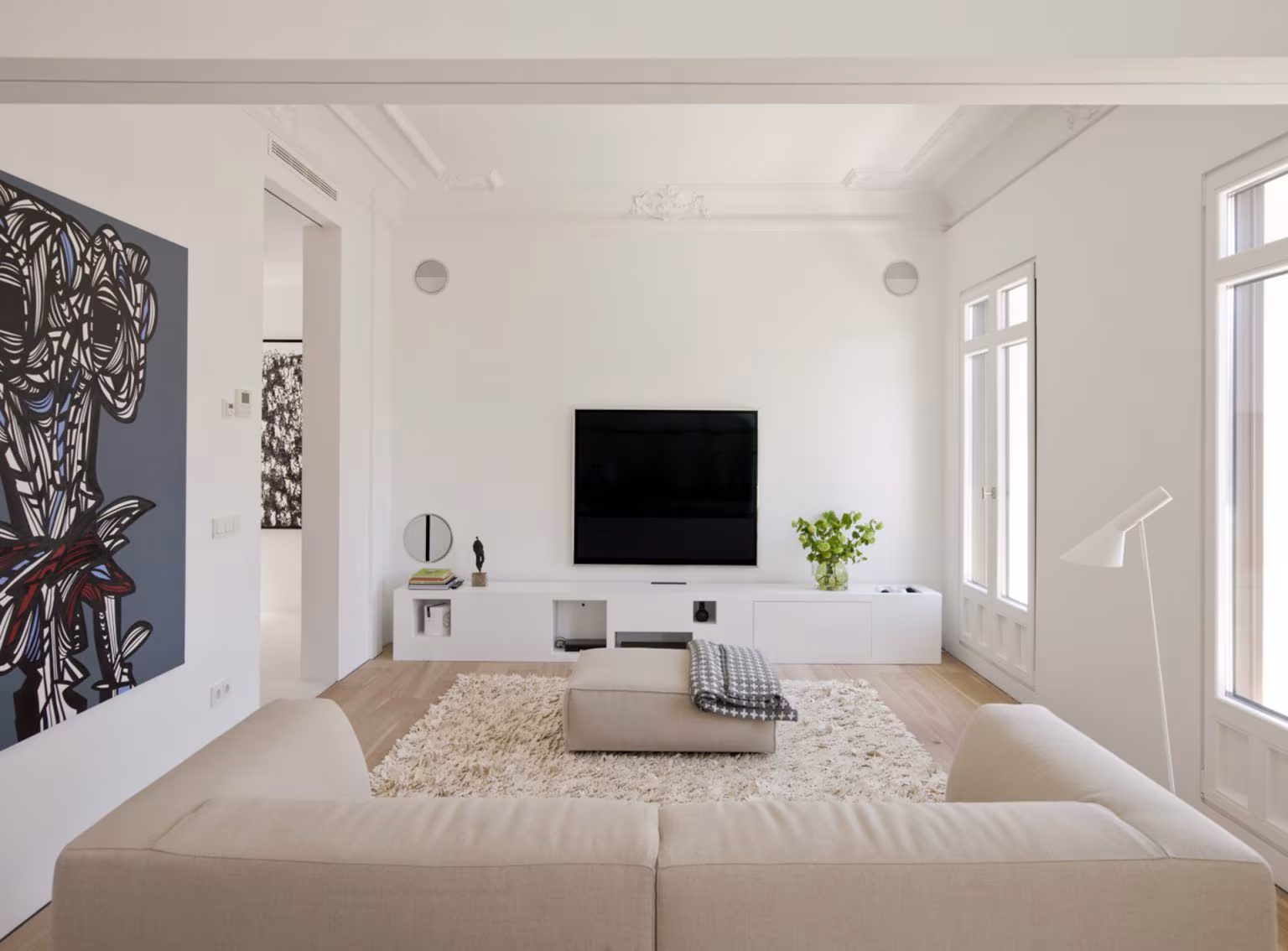 Salón con sofá beige, televisión sobre mueble bajo y cuadro de gran formato bajo molduras, en Alcalá