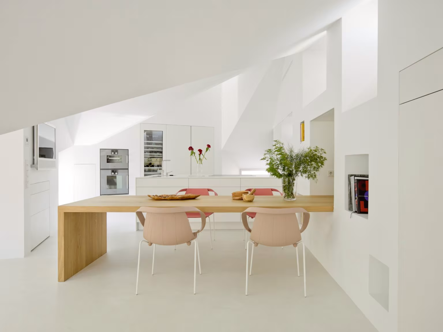 Cocina y comedor con mesa de roble, sillas rosadas y cubierta blanca de planos inclinados, en Alcalá