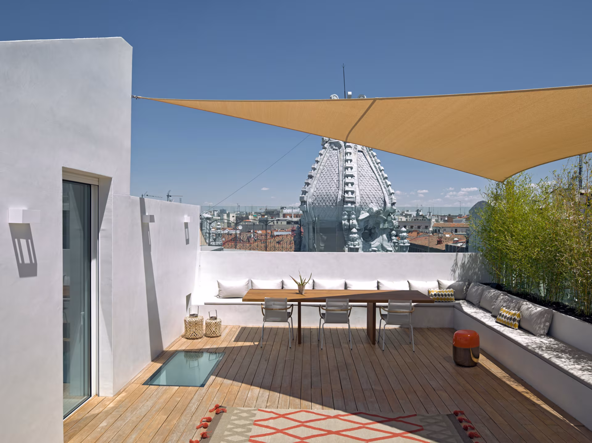 Terraza de cubierta con toldo, mesa de madera, banco corrido y vistas a los edificios de Madrid, en Alcalá