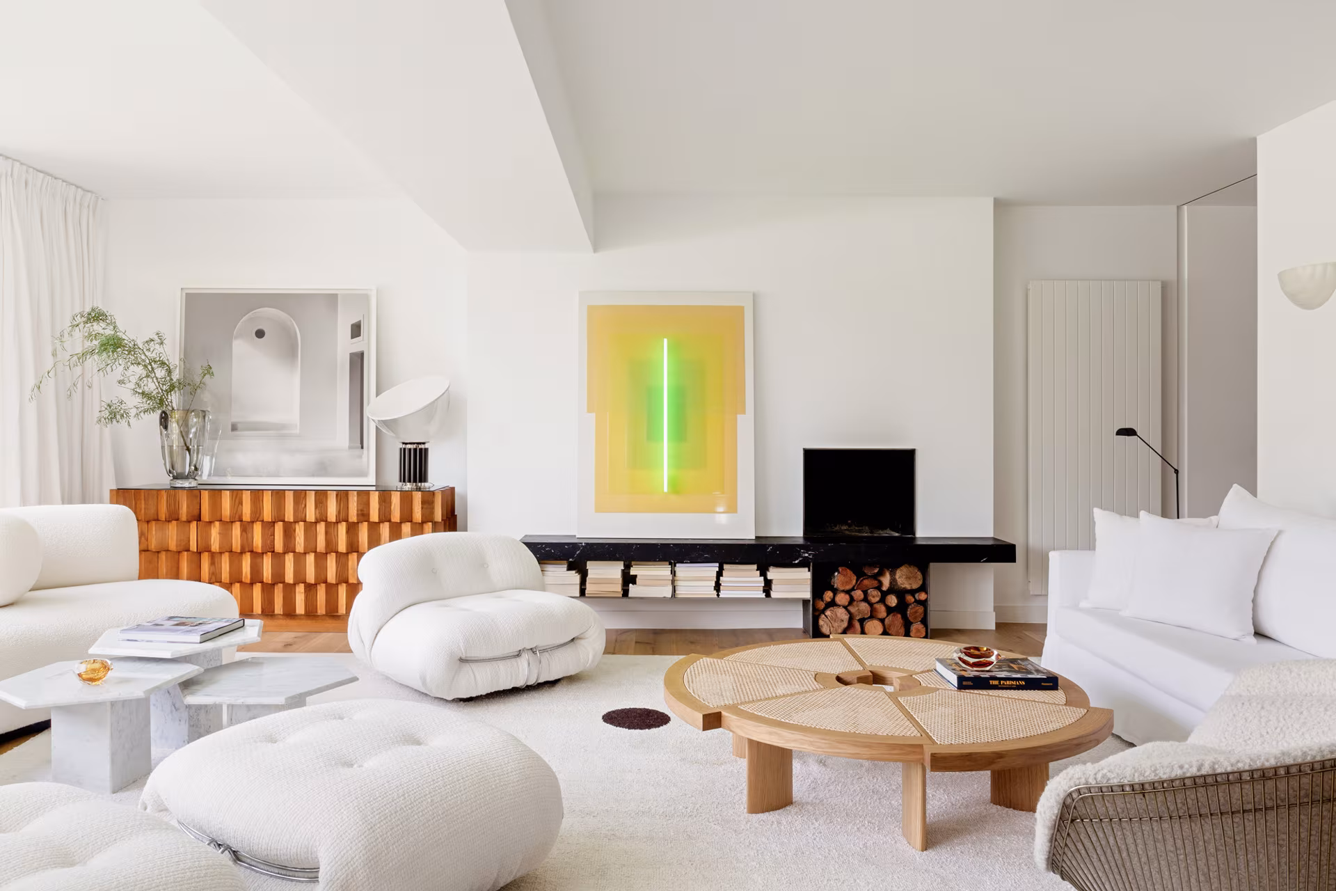 Living room of an Ábaton residence with white bouclé armchairs, a timber sideboard, a fireplace and a neon artwork