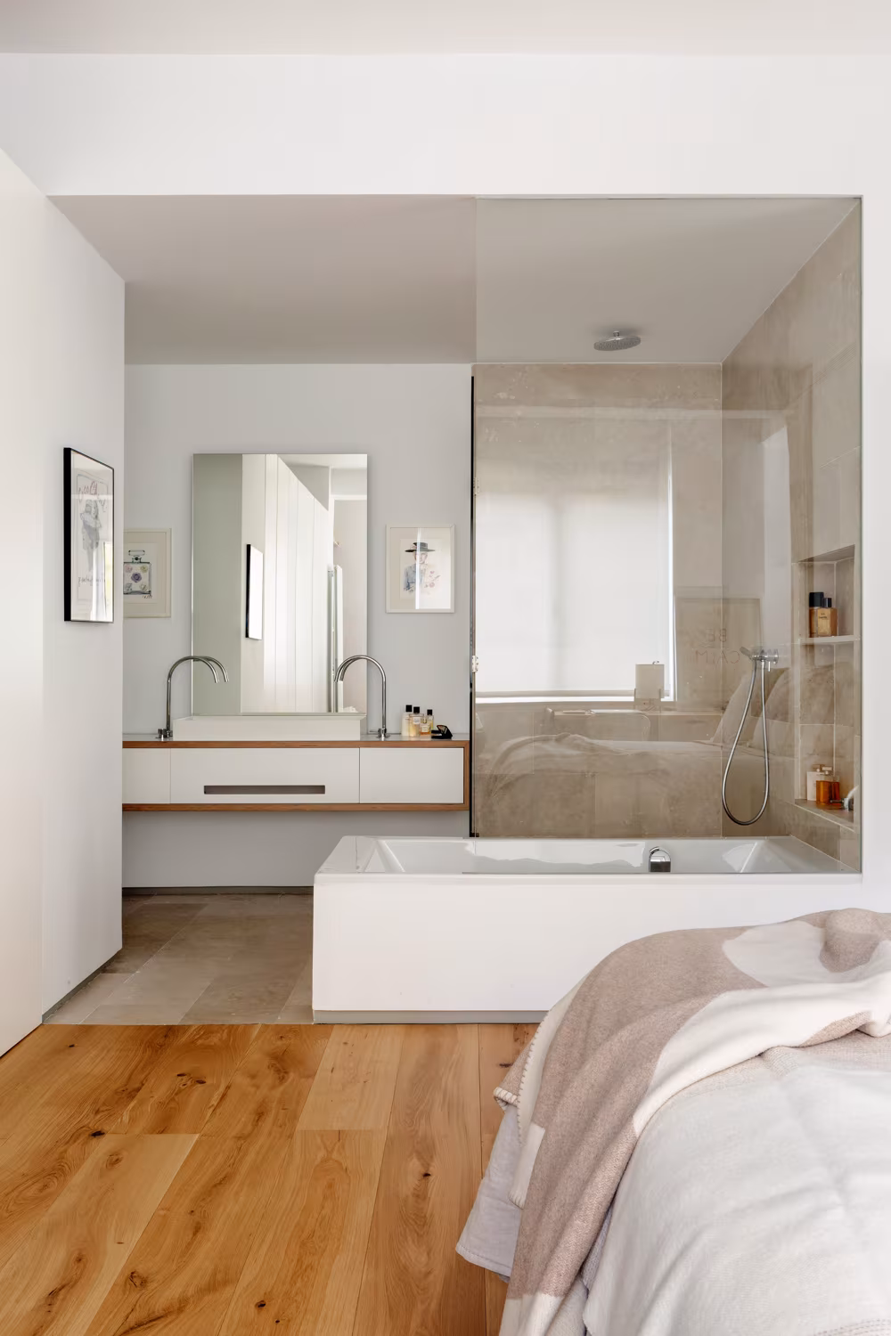 Baño integrado en el dormitorio tras un cristal, con bañera y lavabo doble de madera, en Santiago Bernabéu
