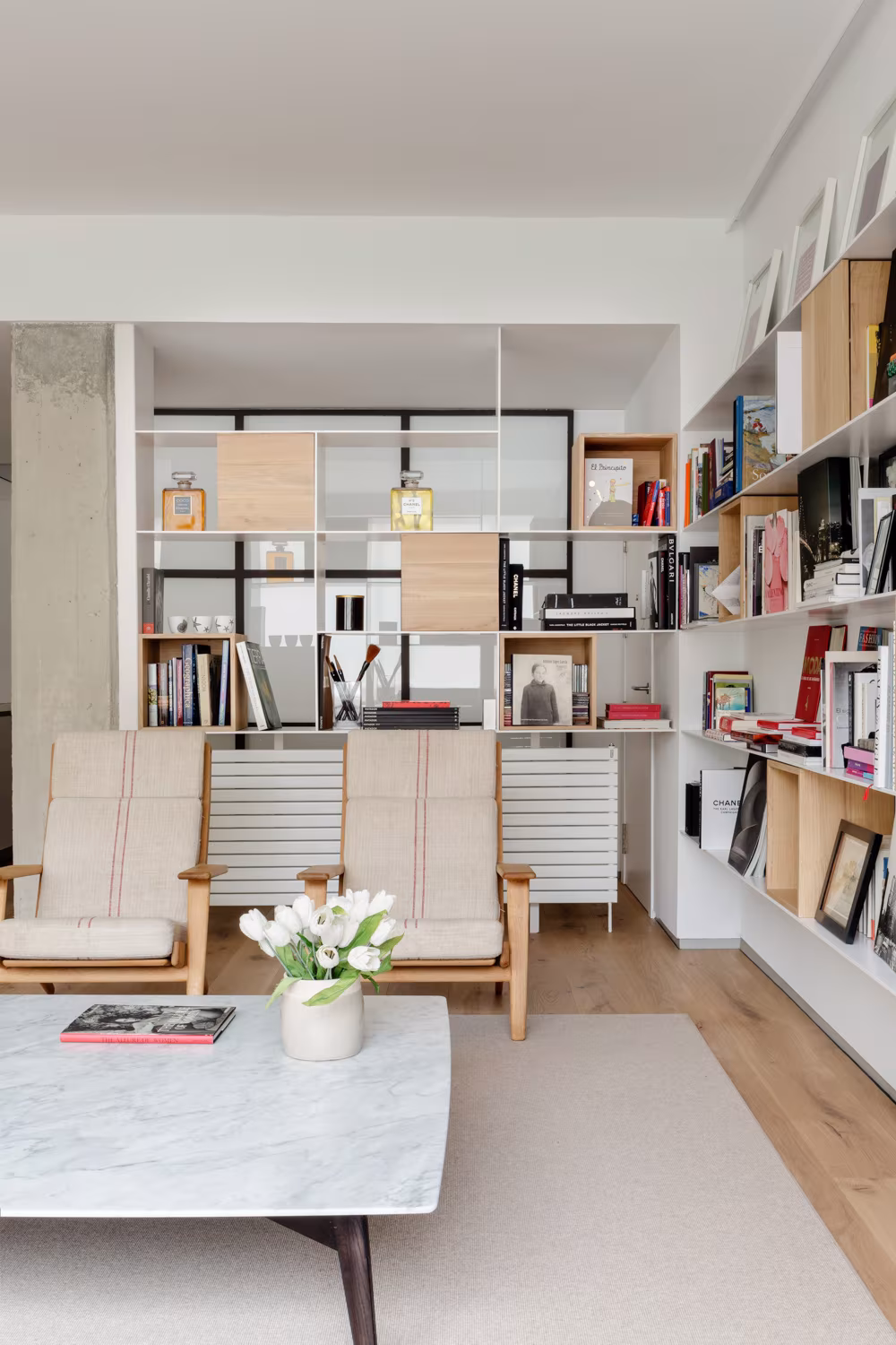 Estancia con pilar de hormigón, librería de módulos blancos y butacas de madera, en la reforma de Santiago Bernabéu