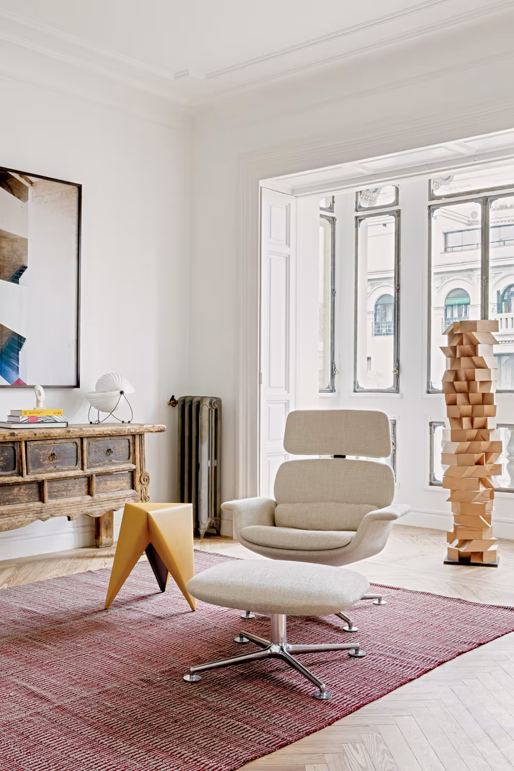 Room with a white lounge chair, burgundy rug and a timber block sculpture before moulded balcony windows, Casa Ayala II