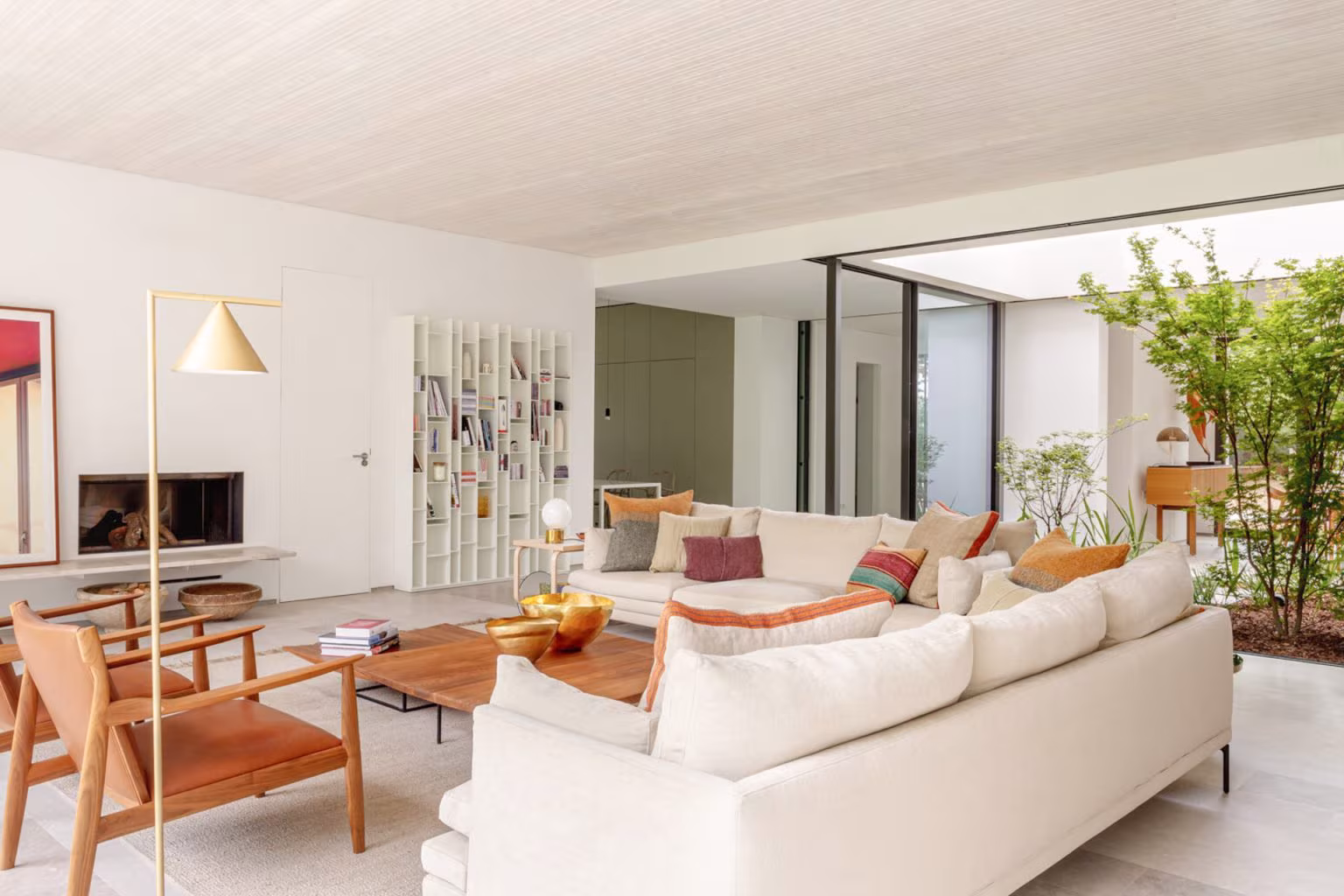 Living room in the LVL refurbishment with white sofa, timber armchairs and fireplace beside the glazed courtyard