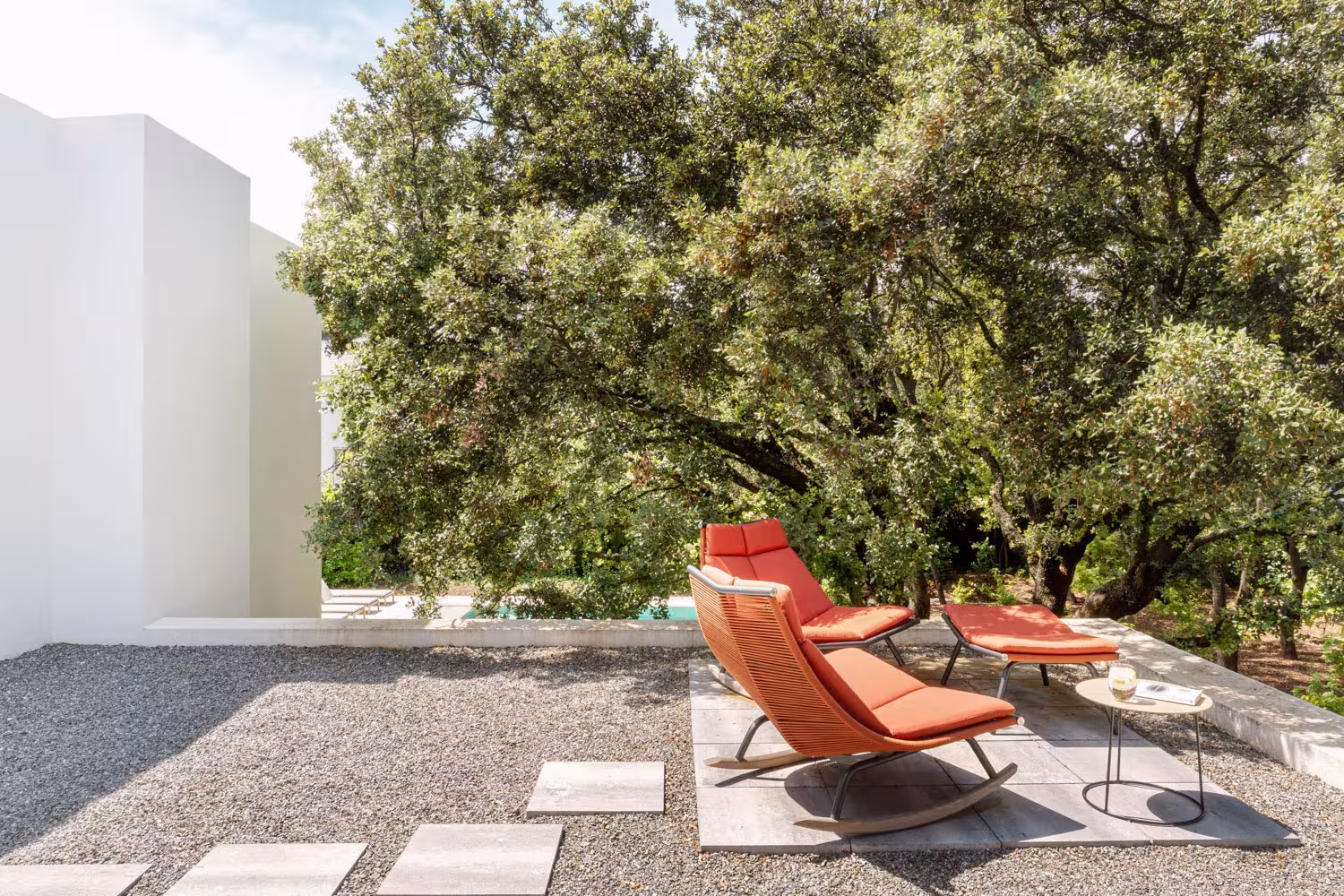 Gravel terrace with stepping stones and orange loungers beneath holm oaks, LVL refurbishment, Madrid