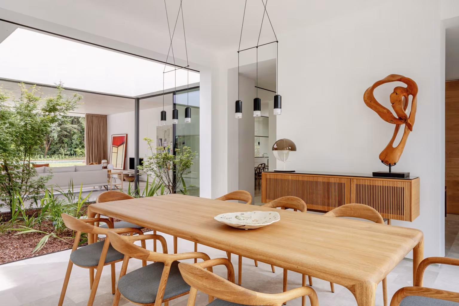 Dining room with timber table and oak sculpture facing a planted courtyard, LVL refurbishment, Madrid
