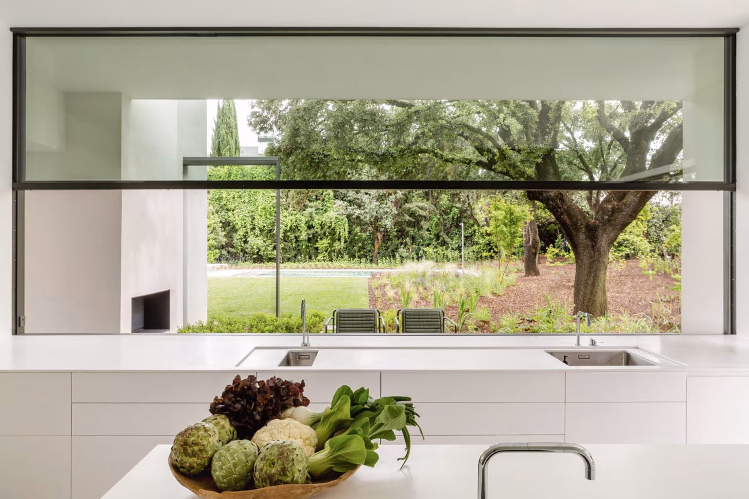 Wide window above the kitchen worktop framing an oak tree and lawn, LVL refurbishment, Madrid