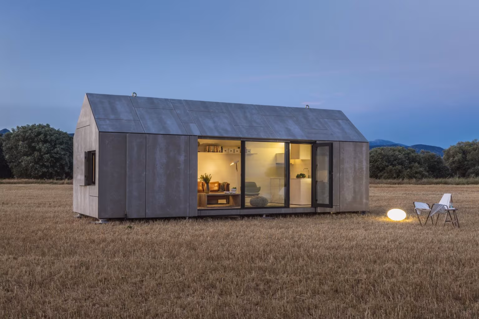Cabaña de madera iluminada al anochecer en un prado, imagen del proyecto ARV8 de Ábaton