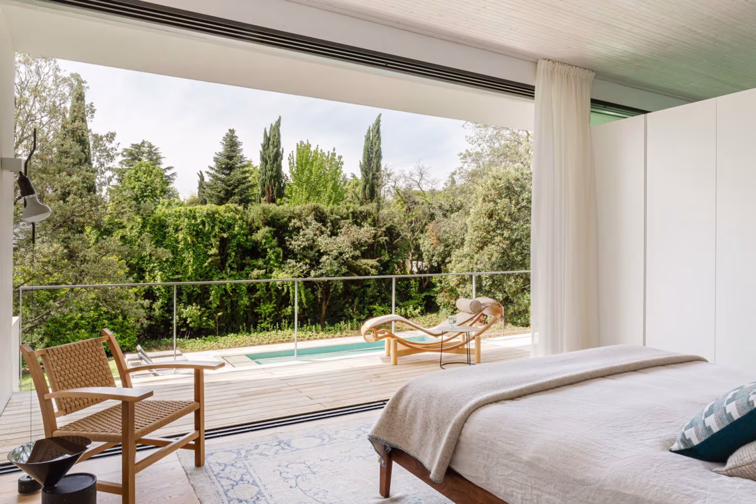 Bedroom opening through sliding glazing to a terrace and pool among cypresses, LVL refurbishment