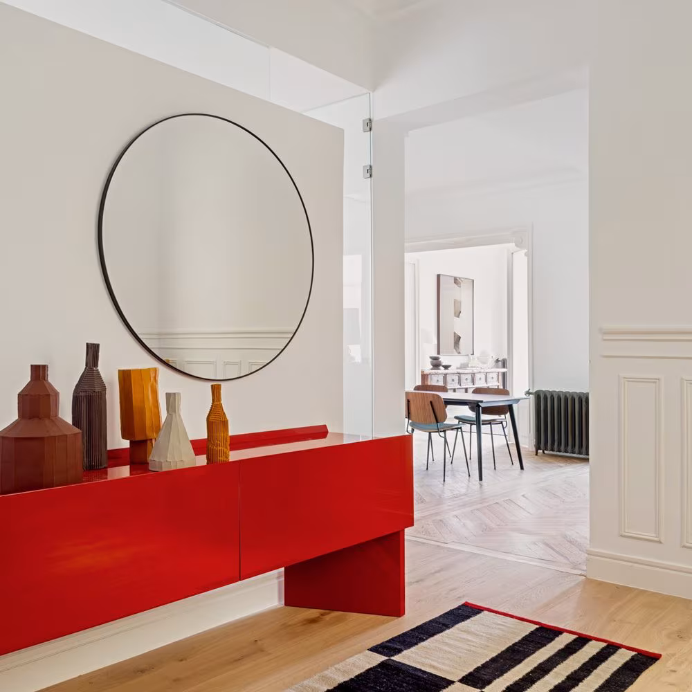 Recibidor de la reforma Sagasta II de ÁBATON con mueble rojo lacado, espejo redondo y jarrones