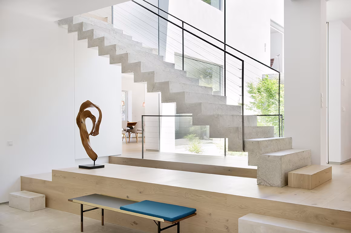 Escalera de hormigón con barandilla de cristal y escultura de madera sobre una tarima de roble en Casa L de Ábaton