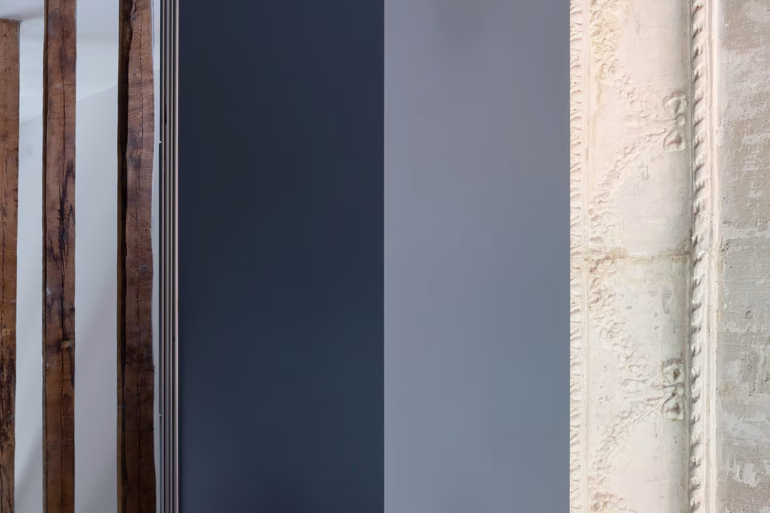 Detail of timber beams, a dark panel and a concrete wall with exposed rebar