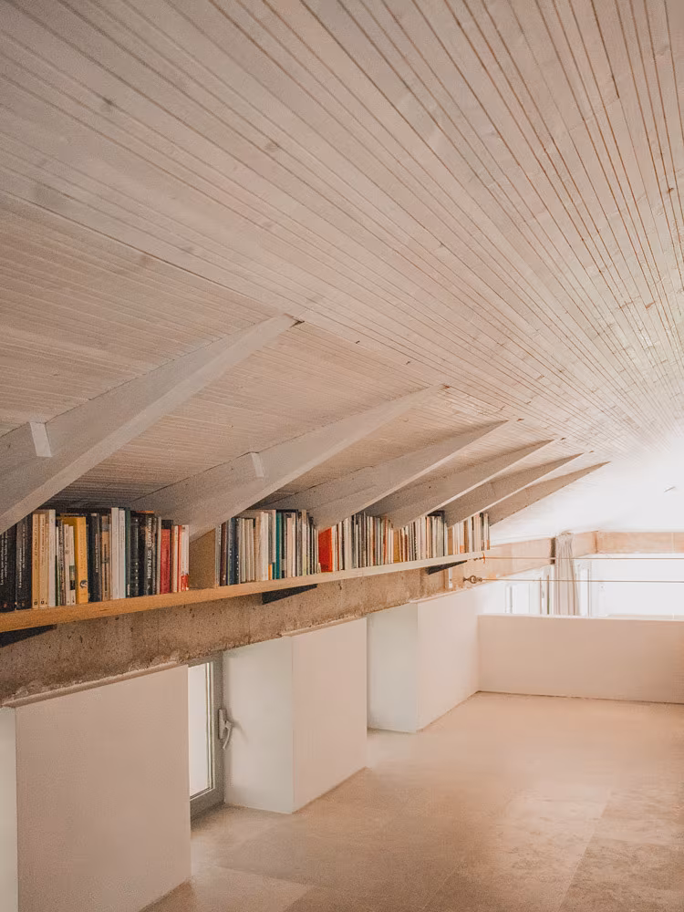 Attic with a sloping timber-board ceiling and a bookshelf of books beneath the rafters