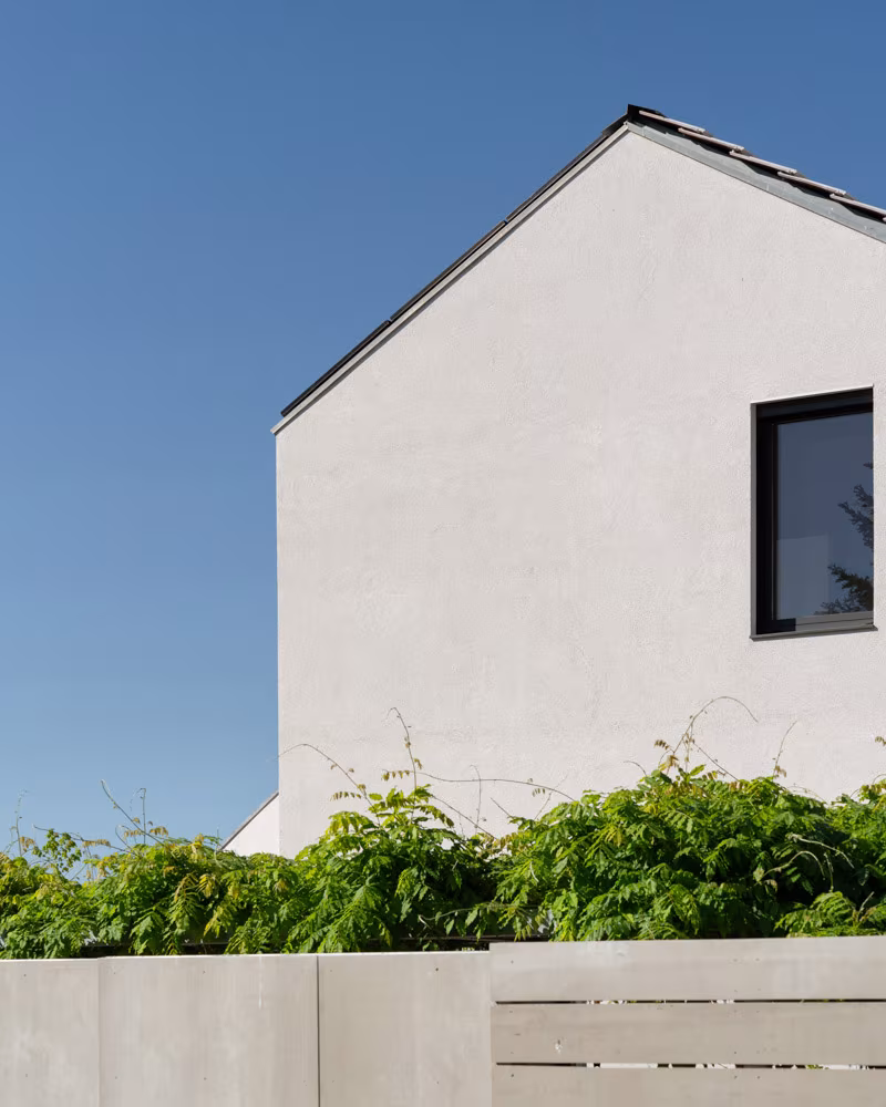 White gabled facade with a window and foliage above the garden wall against a blue sky