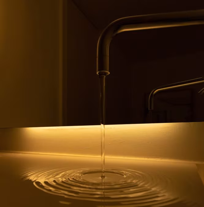 Bronze tap with a thread of water falling into a basin lit by warm light