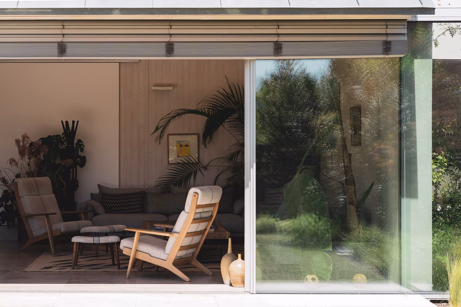 Living room with wooden armchairs opening through a sliding glass door onto a lush garden