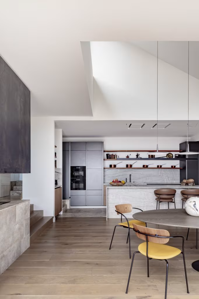 Cocina contemporánea con isla de mármol, muebles grises y estantes con menaje de cobre