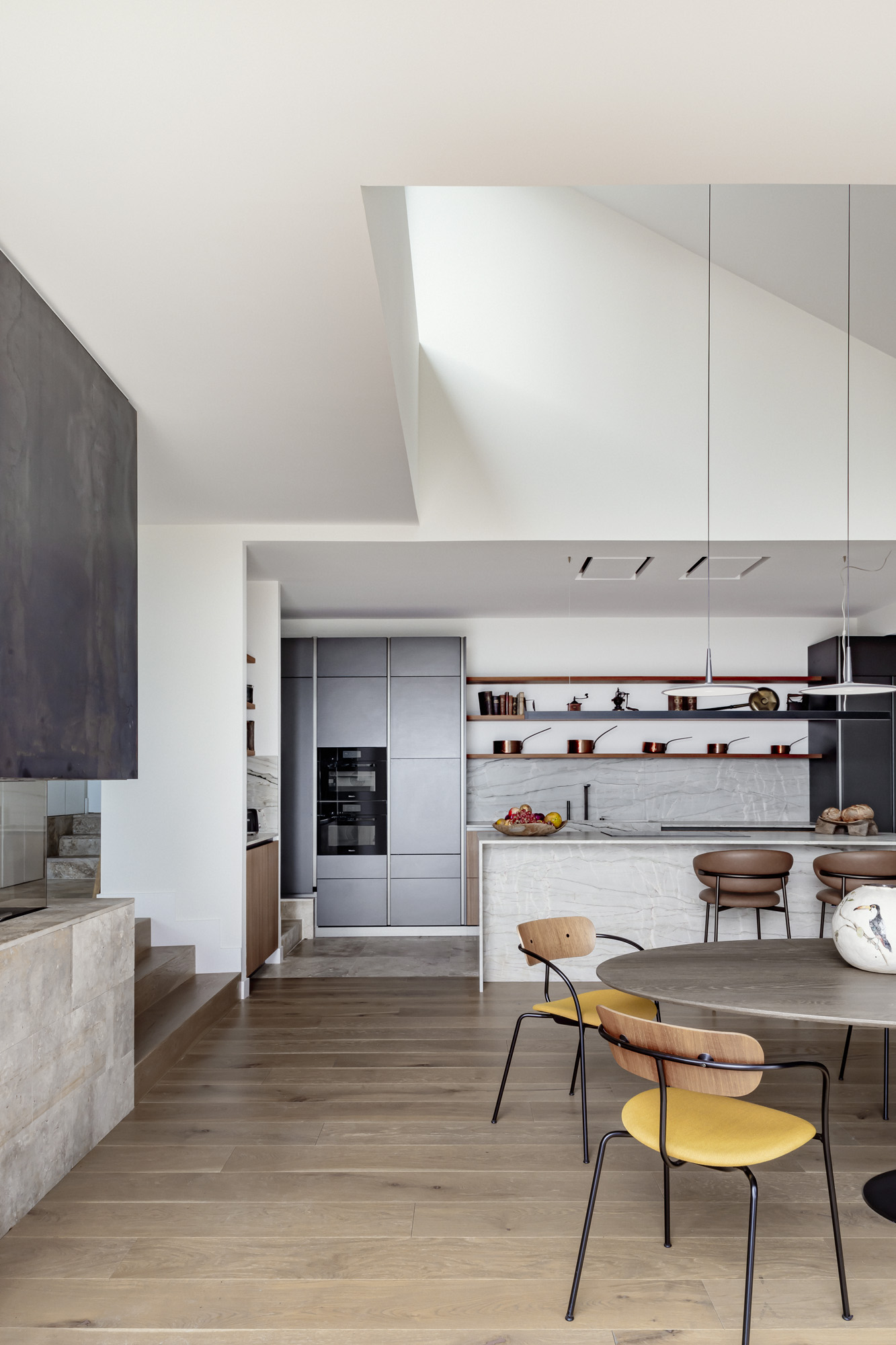 EL ESCORIAL- 45 Cocina contemporánea con isla de mármol, mobiliario en tonos grises, estanterías lineales con menaje de cobre, comedor minimalista con suelo de madera natural y sillas y mesa de diseño moderno