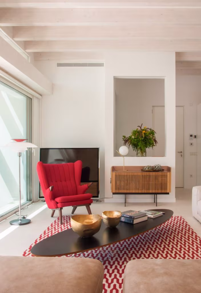 Salón con hornacina, aparador de lamas de roble, butaca roja y mesa baja ovalada negra en Casa JP, Madrid