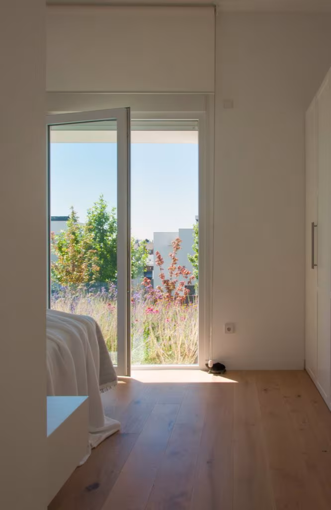 Dormitorio con puerta de vidrio abierta a una pradera de gramíneas y suelo de roble en Casa JP, Madrid