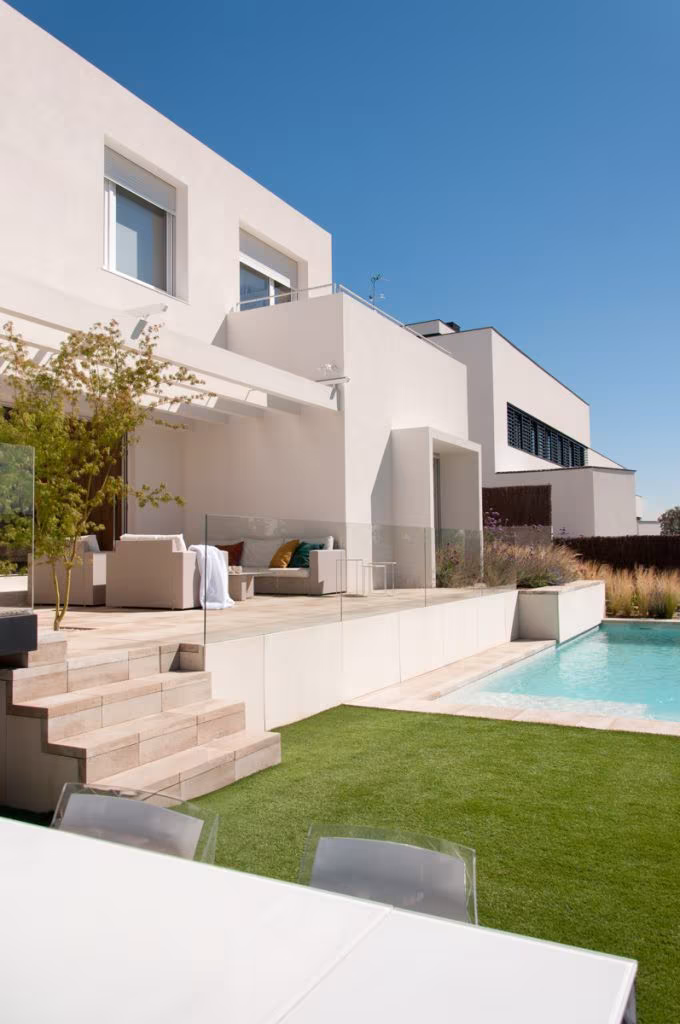 Terraza con escalones de madera, piscina y fachada blanca de Casa JP con criterio bioclimático, Madrid
