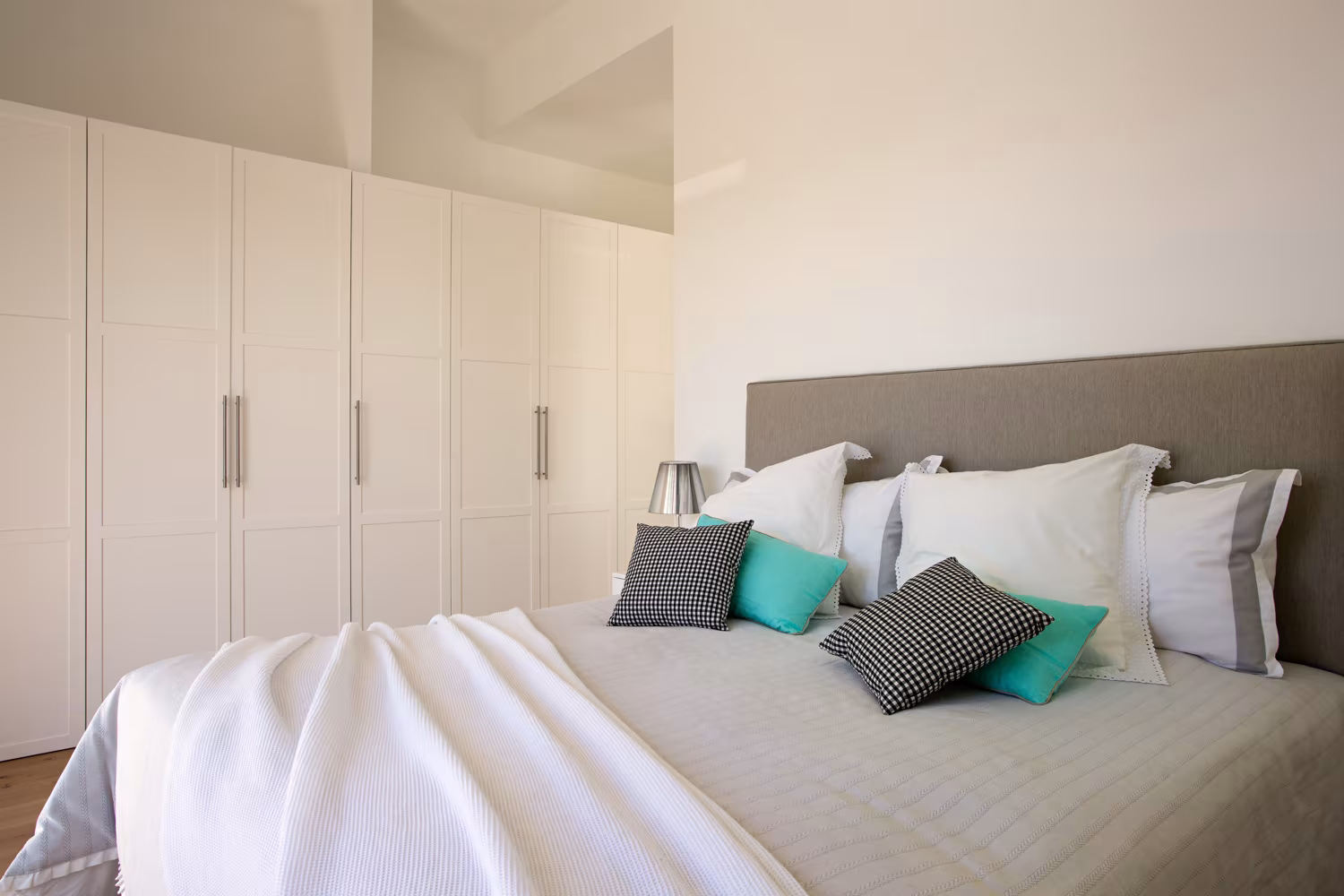 Dormitorio de Casa JP con armarios blancos empotrados, cabecero gris y cojines estampados