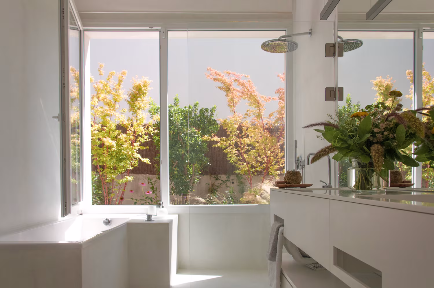 Baño con bañera blanca y encimera ante una ventana abierta a un jardín con plantas otoñales en Casa JP