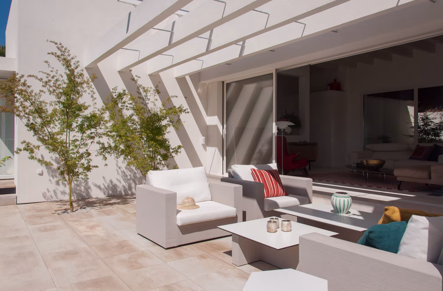 Terraza con celosía blanca, sofás de exterior y árboles jóvenes abierta al salón en Casa JP, Madrid