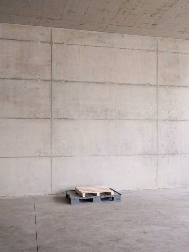 Board-formed exposed concrete wall with a single pallet on the floor of a CVNE winery hall