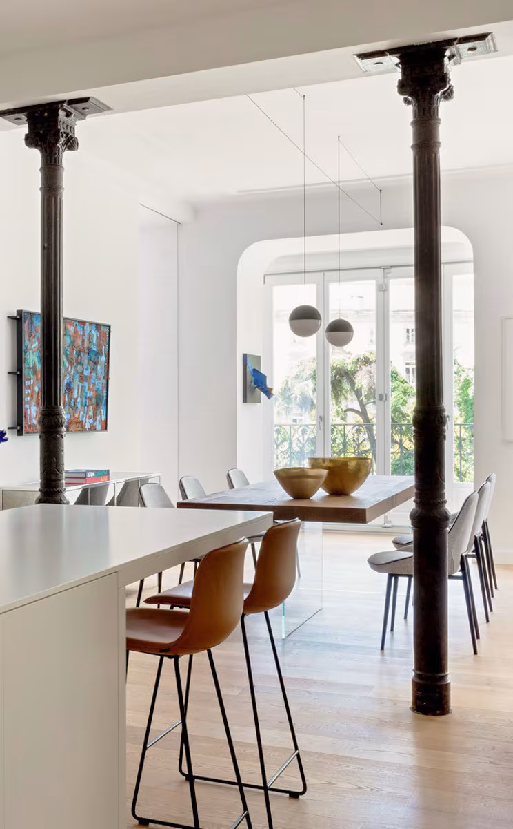 Dining area and kitchen with a white island between cast-iron columns and spherical pendants in an Ábaton residence