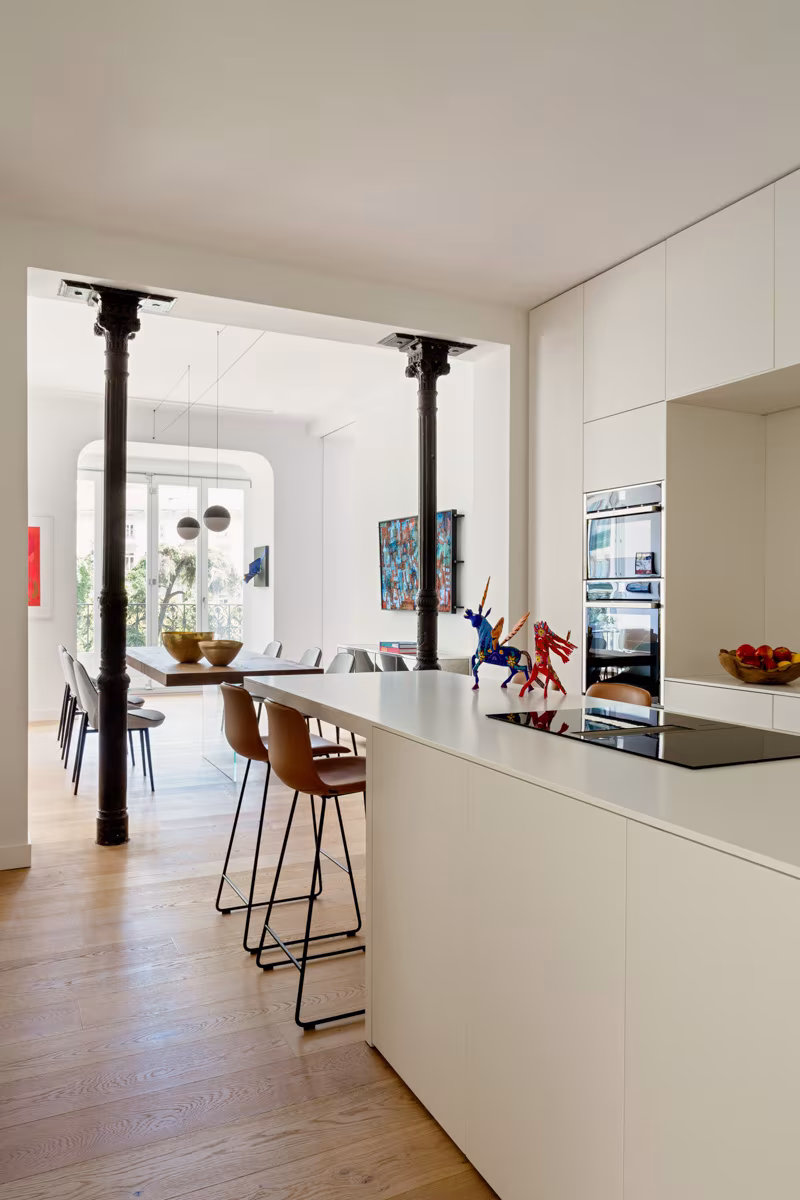 Cocina central con isla blanca, taburetes y columnas negras abierta al comedor en la reforma de Salesas