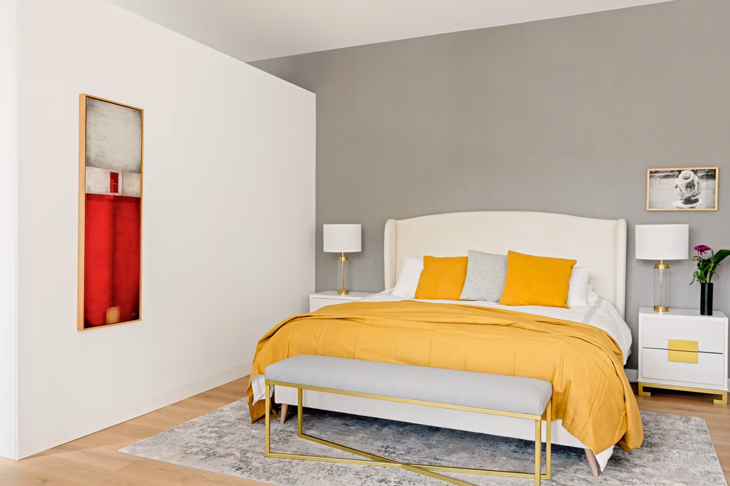Dormitorio con cama de cabecero tapizado, colcha amarilla, banco dorado y pared gris en Salesas, Madrid