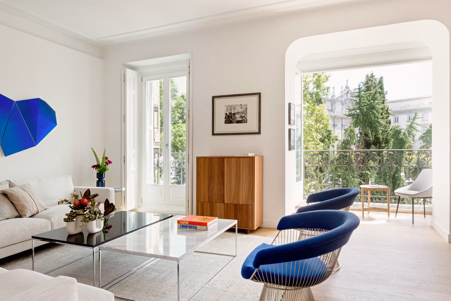 Salón con balcón arqueado, butacas azules de alambre y mesa de cristal en la Reforma Integral en Salesas