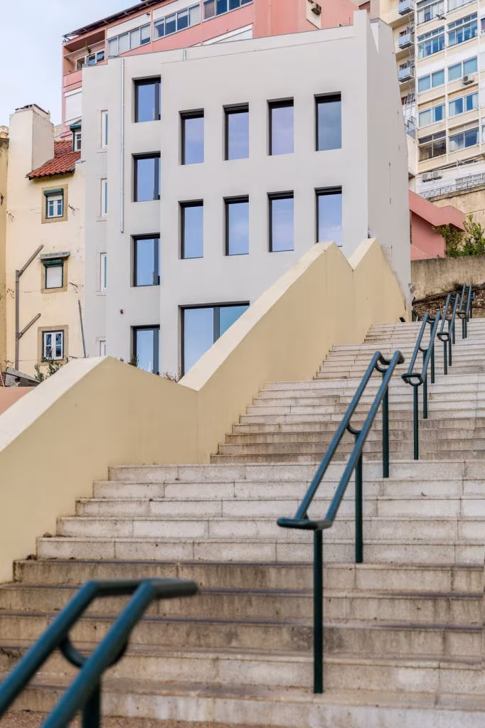 Fachada blanca con ventanas azules sobre una escalera con barandilla verde en el alojamiento de Lisboa