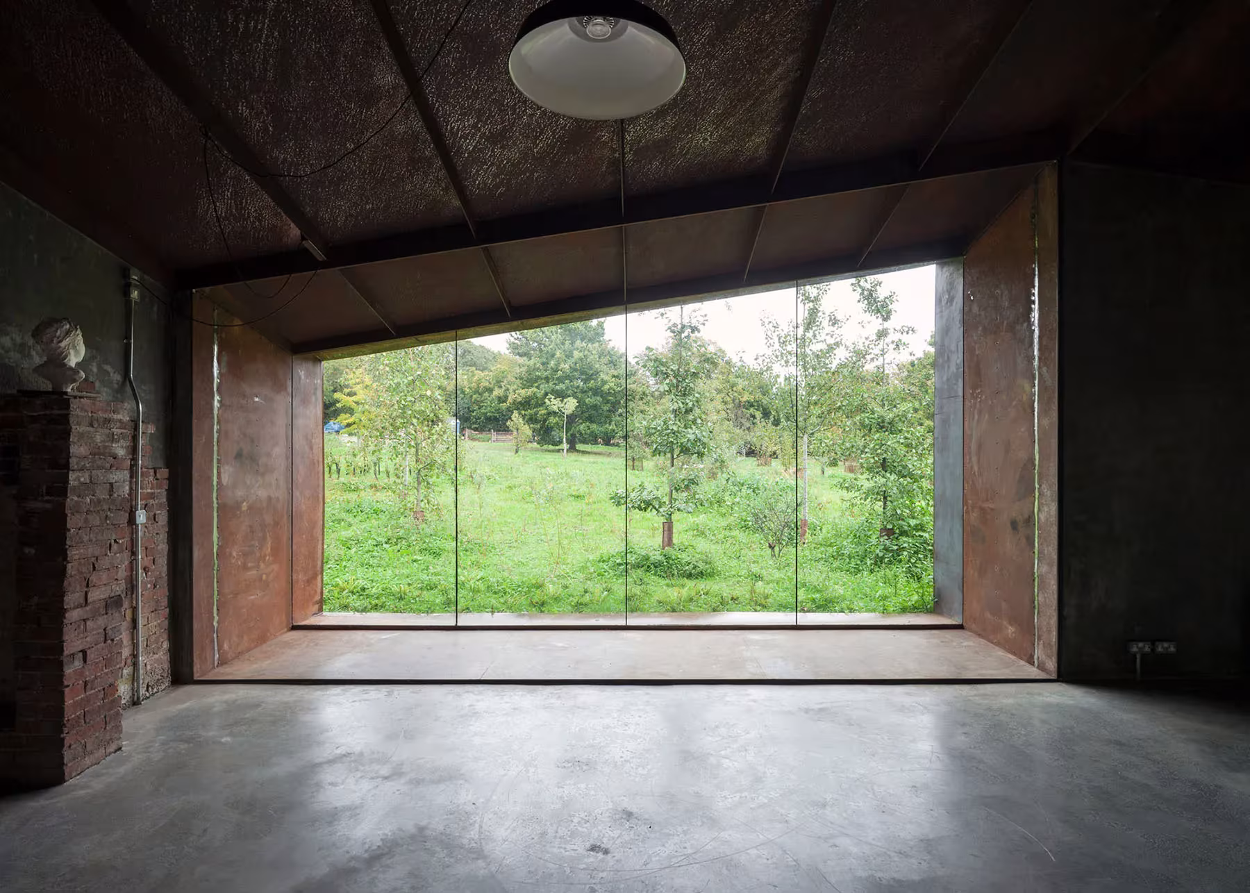 Interior del pabellón de Carmody Groarke con suelo de hormigón y gran ventana abierta al prado