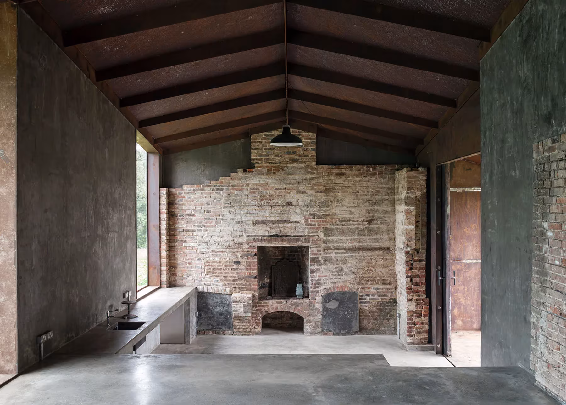 Interior del pabellón de Carmody Groarke con armadura de madera, chimenea de ladrillo y suelo de hormigón