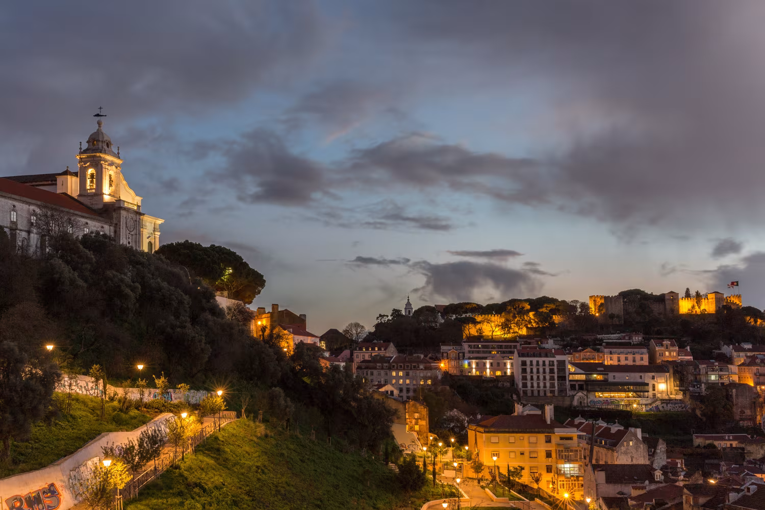 Vista nocturna de Lisboa con la colina del castillo iluminada y una iglesia desde el Alojamiento Singular