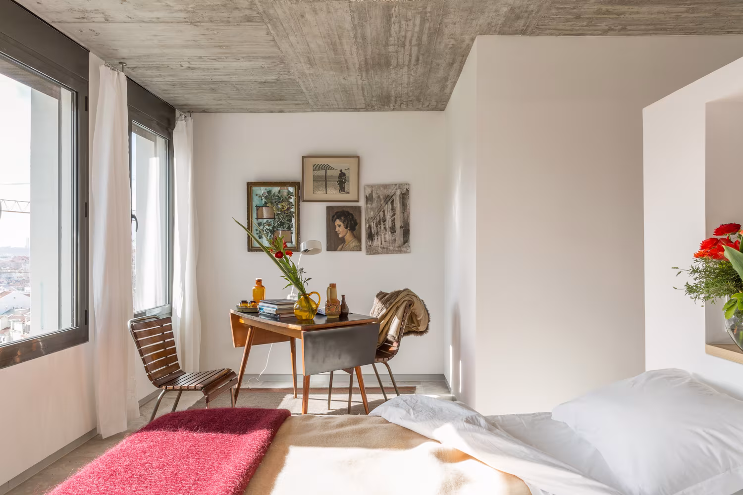 Habitación con escritorio de madera, cuadros pequeños y alfombra rosa bajo techo de hormigón en Lisboa