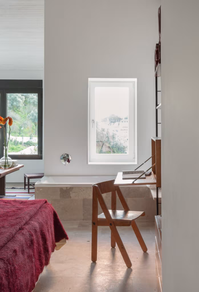 Dormitorio con silla plegable de madera, colcha granate y ventana pequeña al paisaje en el alojamiento de Lisboa