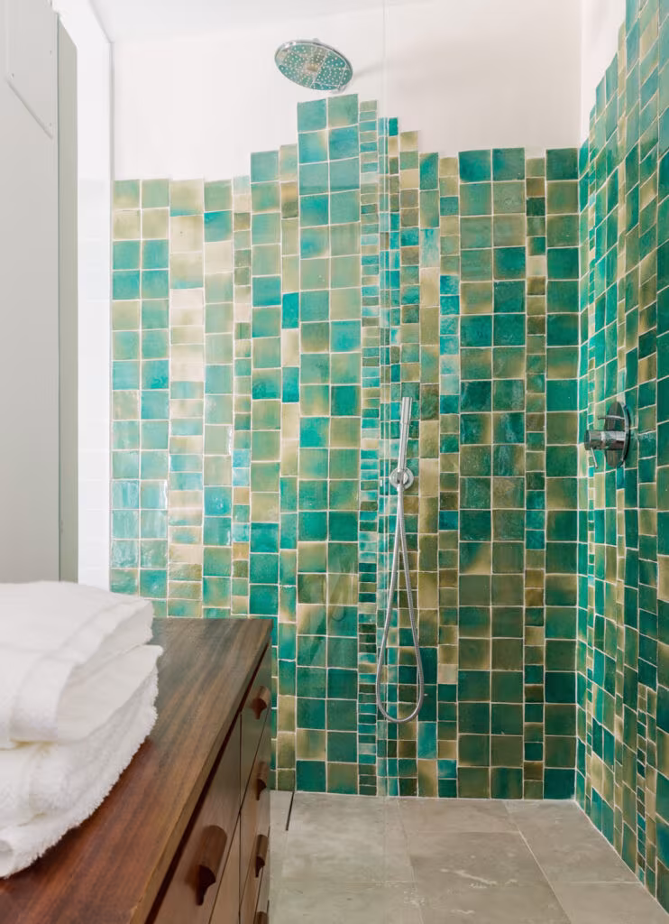 Ducha revestida de azulejos esmaltados verdes con cómoda de madera y toallas en el alojamiento de Lisboa