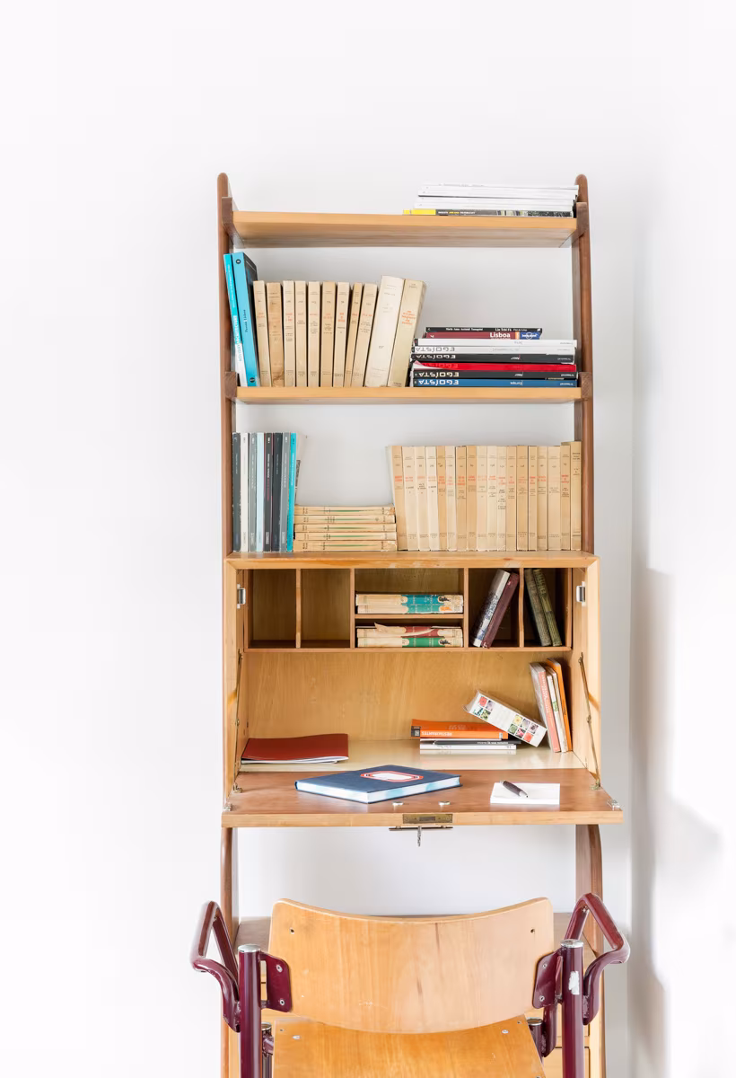 Mueble escritorio de madera con estantes y libros junto a una silla plegable en el alojamiento de Lisboa