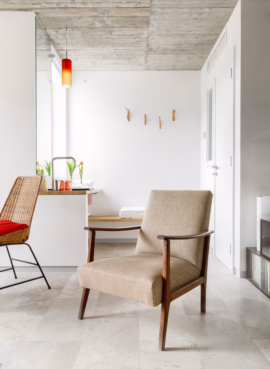 Estancia con butaca de madera de los años 50, cocina compacta y techo de hormigón en el alojamiento de Lisboa