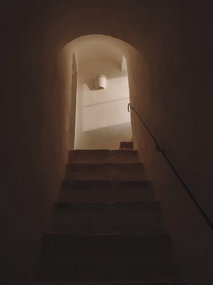 Escalera en penumbra bajo un arco con barandilla metálica oscura en la Casa Casolare Scarani